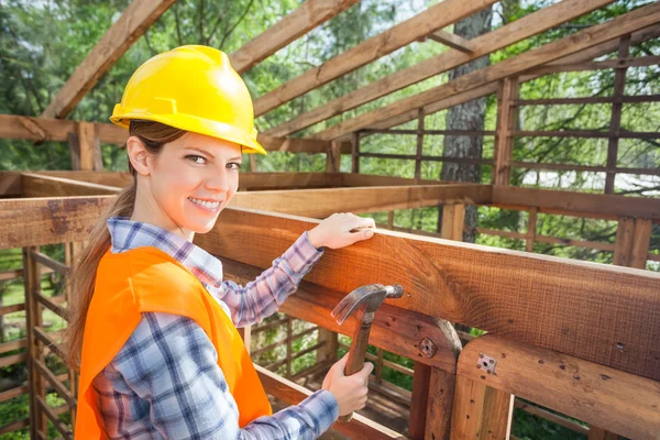 Happy kvinnlig arbetare Hamra spik på Timber Frame — Stockfoto