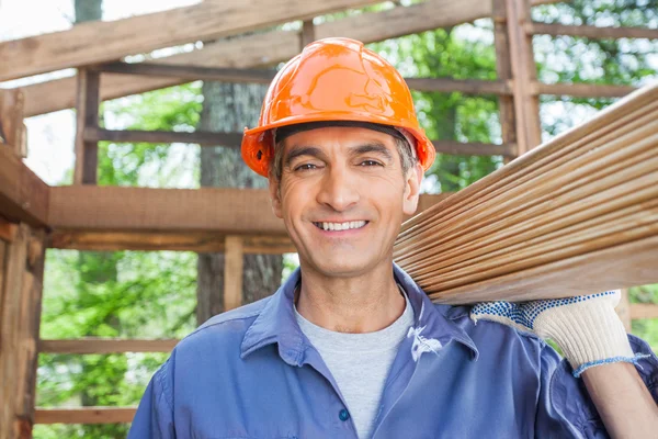 Travailleur de la construction heureux portant des planches en bois — Photo