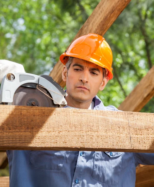 Будівельник використовує електричну пилку на дерев'яній рамі — стокове фото