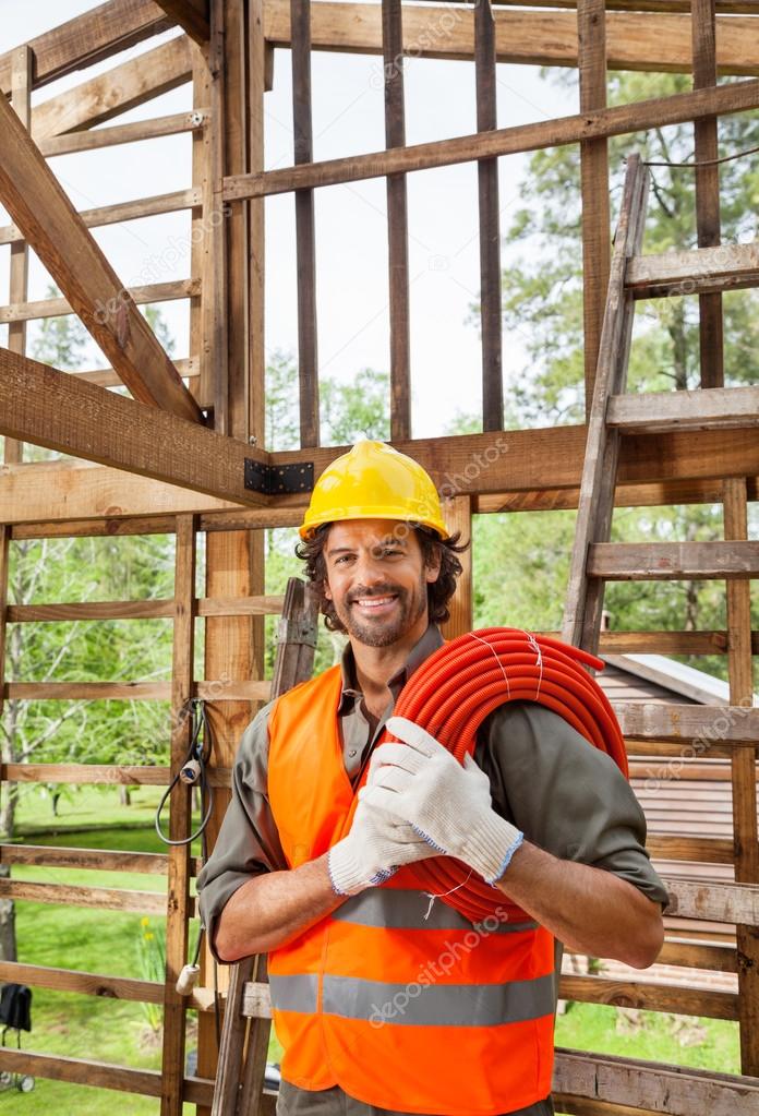 Happy Worker Holding Pipe In Incomplete Wooden Cabin