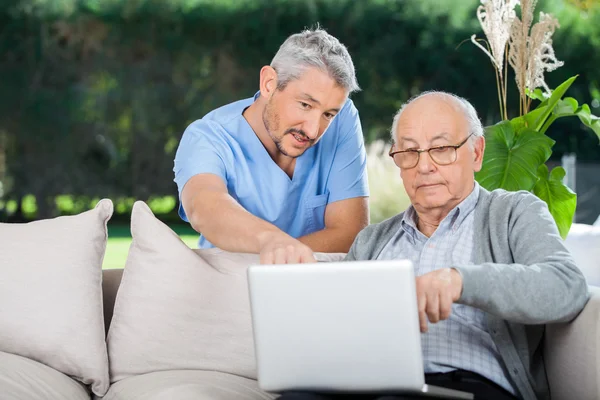 Enfermeira explicando algo no laptop para o homem sênior — Fotografia de Stock