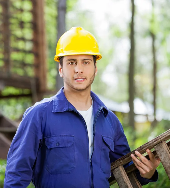 Selbstbewusster Arbeiter trägt Leiter auf Baustelle — Stockfoto