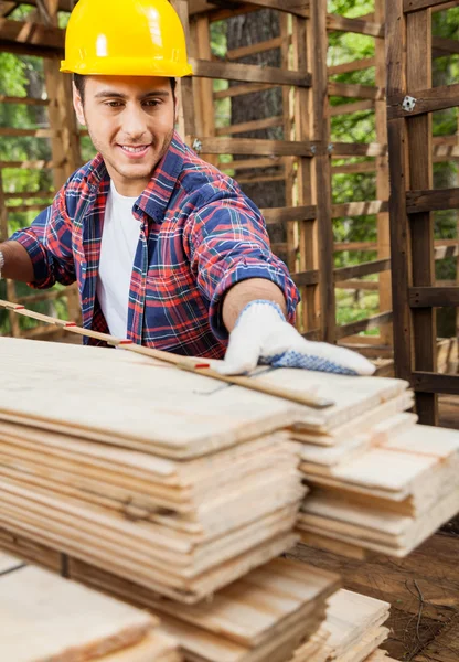 Trabajador que mide el tablón de madera en la cabina en sitio — Foto de Stock