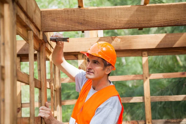 Dělník, zatloukání hřebíku na dřevěnou chatu — Stock fotografie