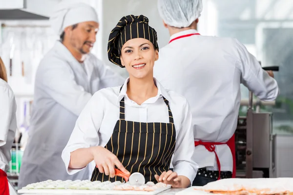 Chef feliz cortando Ravioli Pasta com colegas no fundo — Fotografia de Stock