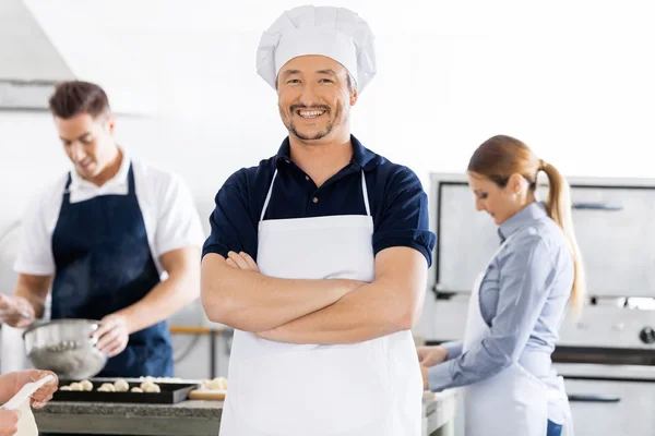 Fiducioso chef in piedi braccia incrociate mentre i colleghi che lavorano in — Foto Stock