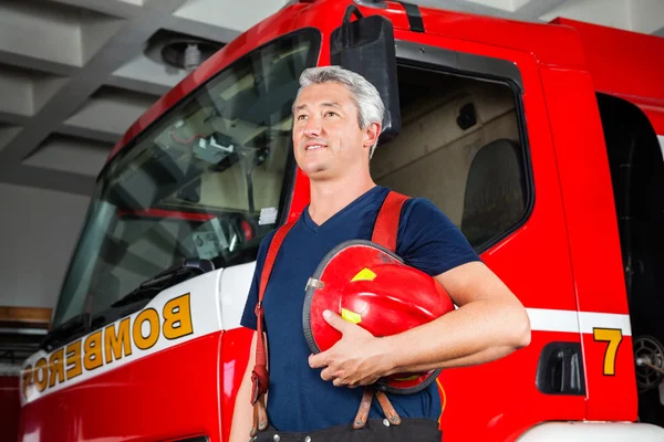 Sorridente pompiere guardando lontano mentre tiene il casco rosso — Foto Stock