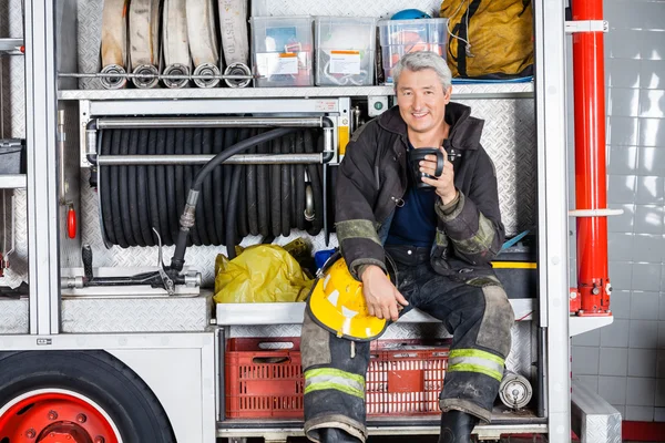 Heureux pompier assis dans le camion à la caserne de pompiers — Photo