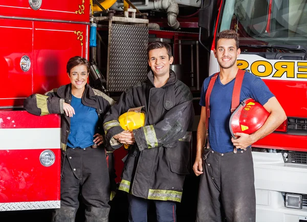 Selbstbewusste junge Feuerwehrleute stehen gegen Lastwagen — Stockfoto