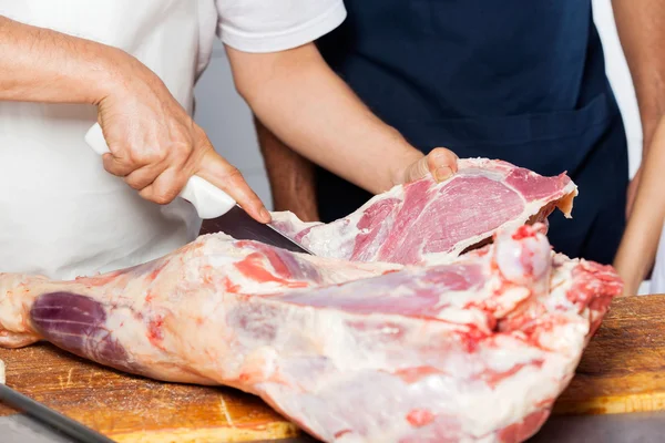 Açougueiro cortando carne por colega no açougue — Fotografia de Stock