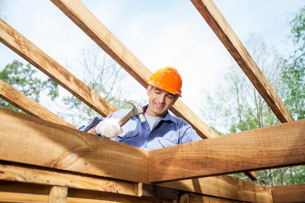 Lavoratore martellante chiodo sulla cabina di legno incompleta in loco — Foto Stock