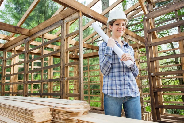 Arquitecto sonriente sosteniendo plano en cabina de madera — Foto de Stock