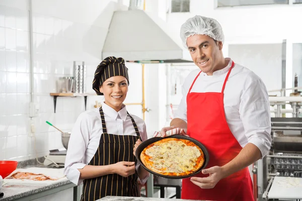 Chefs felizes que apresentam a pizza na cozinha comercial — Fotografia de Stock