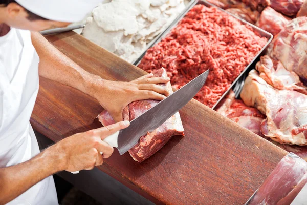 Carniceiro sorridente cortando carne no balcão — Fotografia de Stock