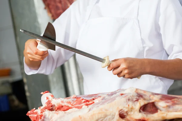 Carniceiro feminino afiando faca no açougue — Fotografia de Stock