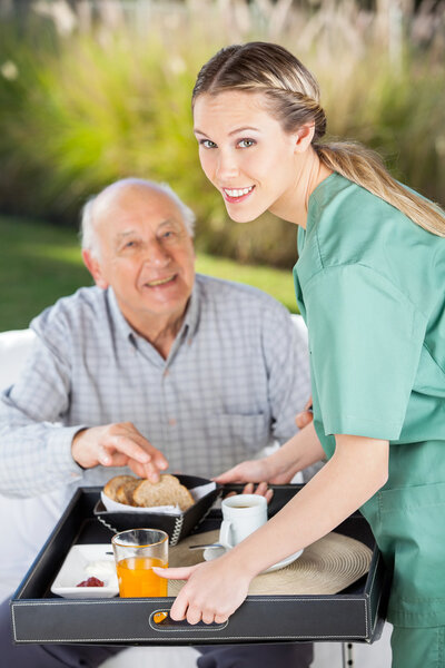 Portrait Of Smiling Female Nurse Serving Breakfast To Senior Man