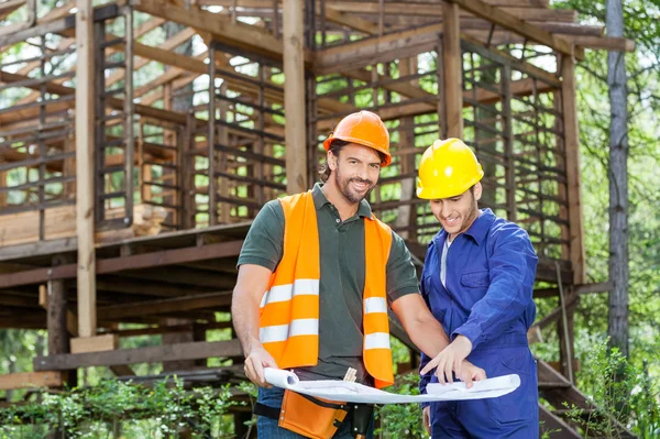 Arquitectos sonrientes con plano en el sitio de construcción — Foto de Stock