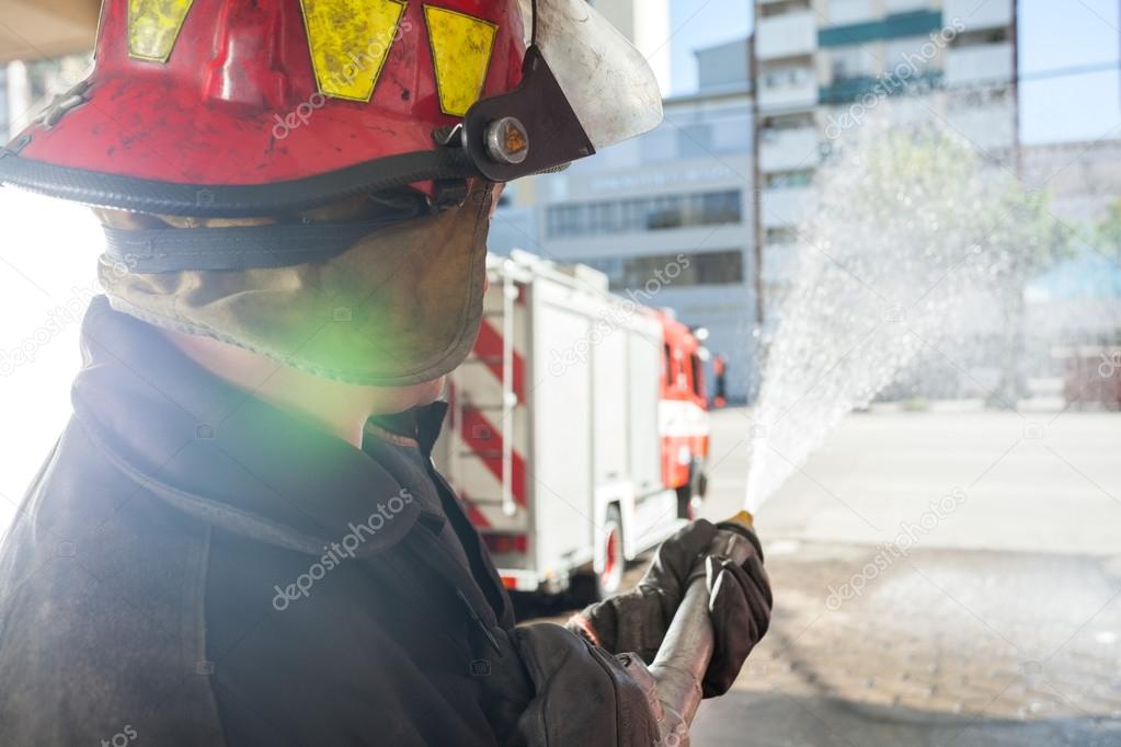 Firefighter Spraying Water While Practicing At Fire Station