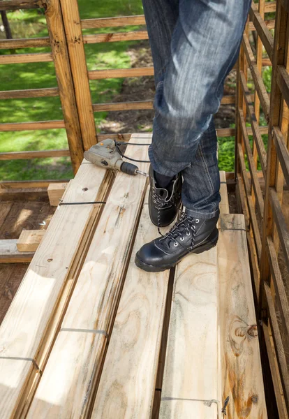 Εργάτης οικοδομών τρυπάνι στις ξύλινες σανίδες για στοιβάζονται στο πλευρό — Φωτογραφία Αρχείου