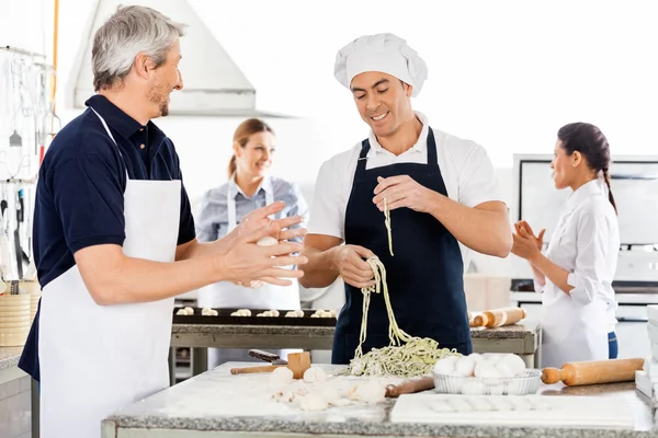 Chefs masculinos e femininos preparando macarrão na cozinha — Fotografia de Stock