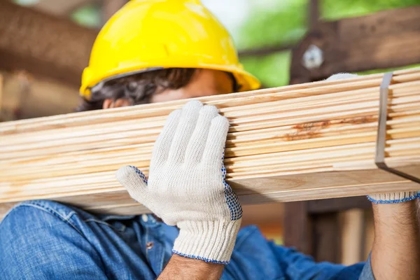 Lavoratore che trasporta assi di legno legati in cantiere — Foto Stock