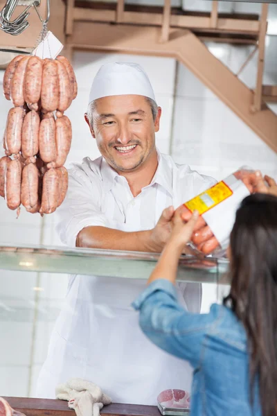 Uomo che dà salsicce imballate al cliente femminile — Foto Stock