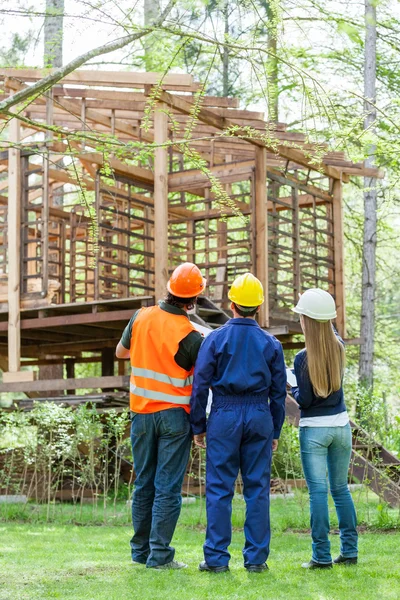 Vista trasera de los arquitectos mirando a la cabaña de madera incompleta — Foto de Stock