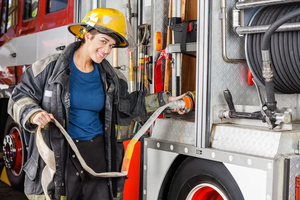 Retrato de feliz bombeiro ajustando mangueira no caminhão — Fotografia de Stock