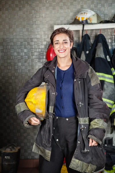 Jovem bombeira segurando capacete no quartel de bombeiros — Fotografia de Stock