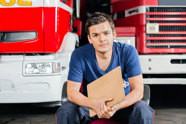 Pompier tenant presse-papiers tout en étant assis contre les camions de pompiers — Photo