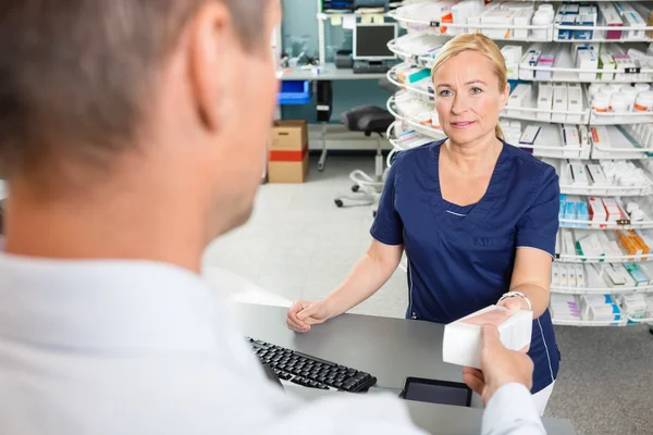 Chimico che dà la scatola della medicina al cliente maschio nella farmacia — Foto Stock