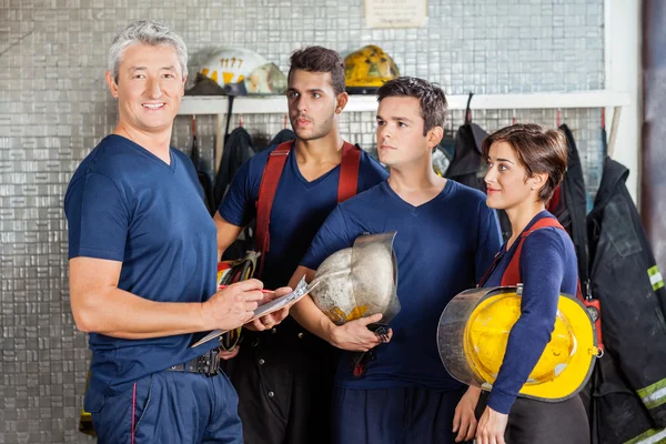 Bombero feliz de pie con el equipo en la estación de bomberos — Foto de Stock