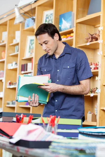 Hombre mirando papeles coloridos en la tienda — Foto de Stock