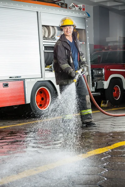 Sonriente bombero rociando agua durante el entrenamiento —  Fotos de Stock