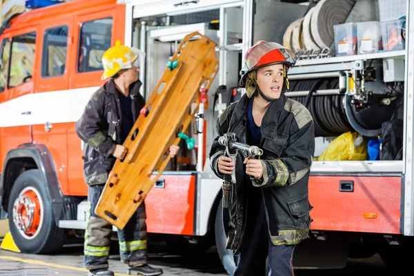 Alarmierter Feuerwehrmann hält Schlauch in der Hand, während Kollege Holzklotz trägt — Stockfoto