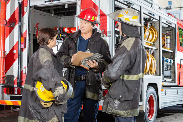 Firefighters Discussing Over Clipboard Against Truck