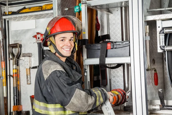 Happy hasič upevnění hadice vody v kamionu — Stock fotografie