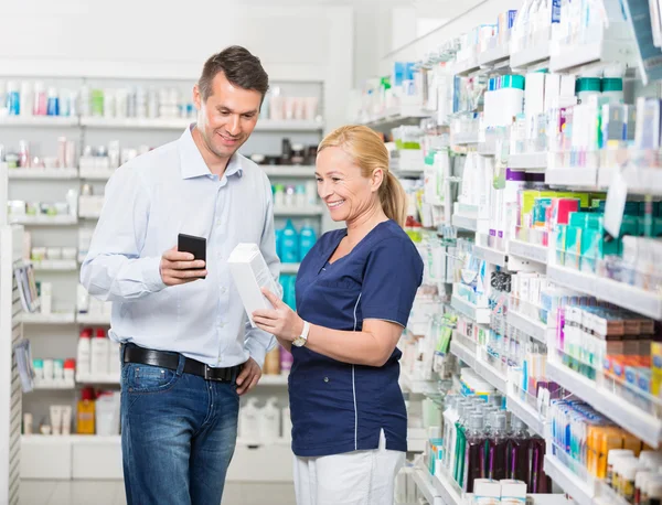 Cliente feliz usando telefone celular enquanto farmacêutico segurando Produ — Fotografia de Stock