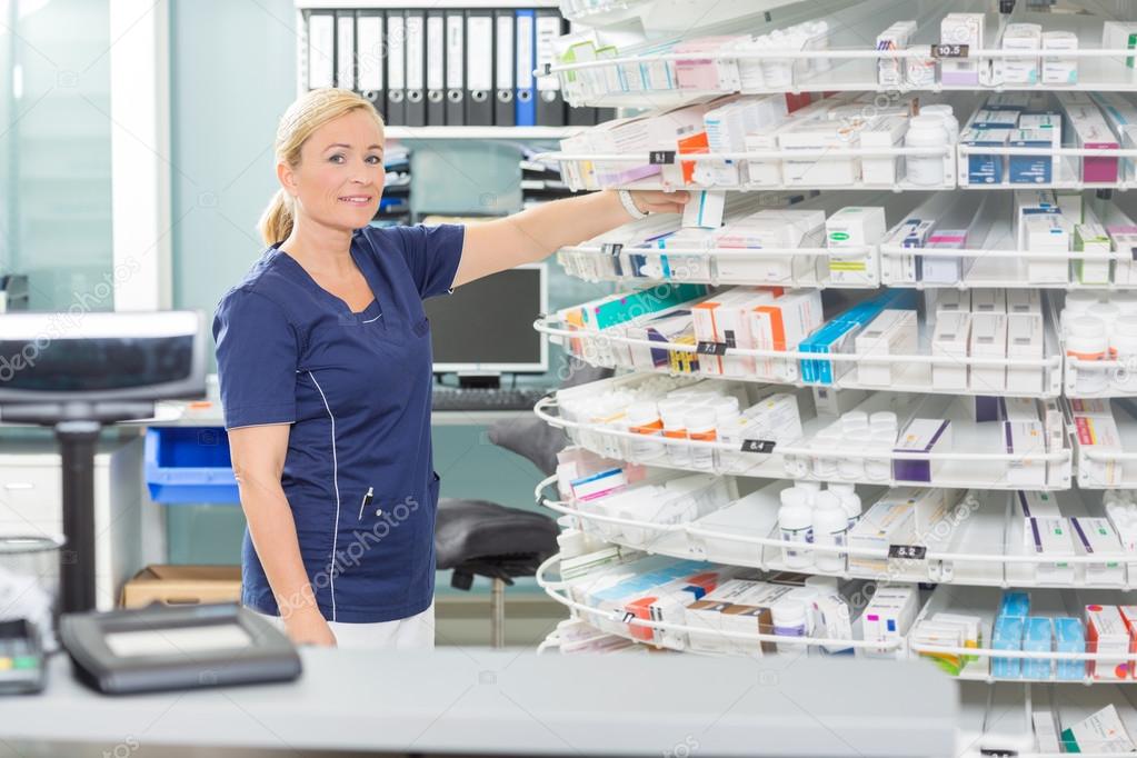 Confident Chemist Arranging Products In Shelves At Pharmacy