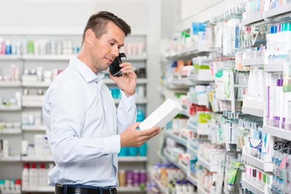 Клієнт використовує мобільний телефон тримаючи продукт в аптеці — стокове фото