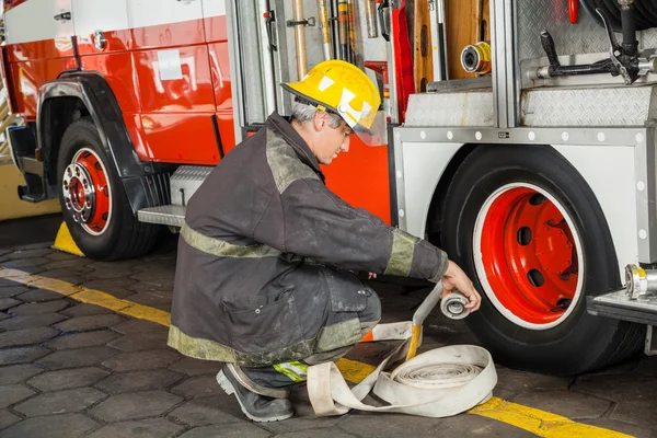 Bombero agachándose mientras sostiene la manguera en camión — Foto de Stock