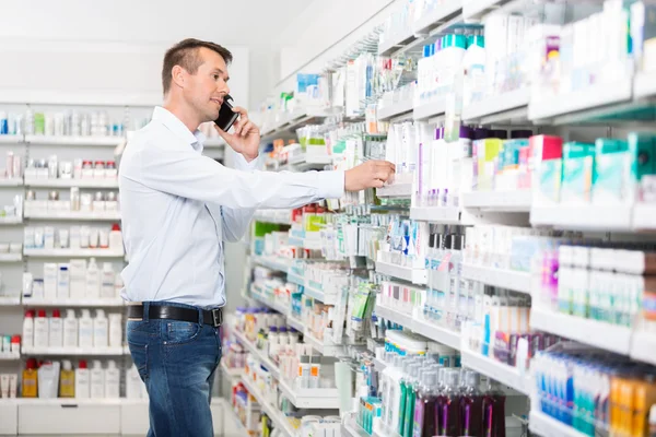 Homem que usa o telefone móvel ao selecionar o produto na farmácia — Fotografia de Stock