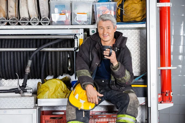 Lächelnder Feuerwehrmann sitzt in LKW am Feuerwehrhaus — Stockfoto