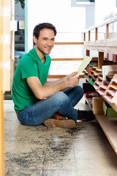 Zákazník drží papír zatímco sedí na podlaze v obchodě — Stock fotografie