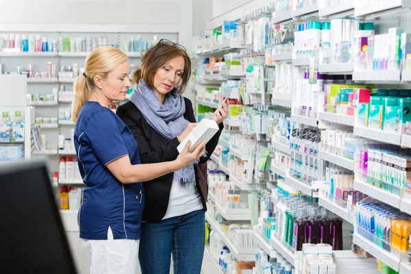 Βοηθός που δείχνει το προϊόν σε γυναίκα, κρατώντας το κινητό στο Pharmac — Φωτογραφία Αρχείου