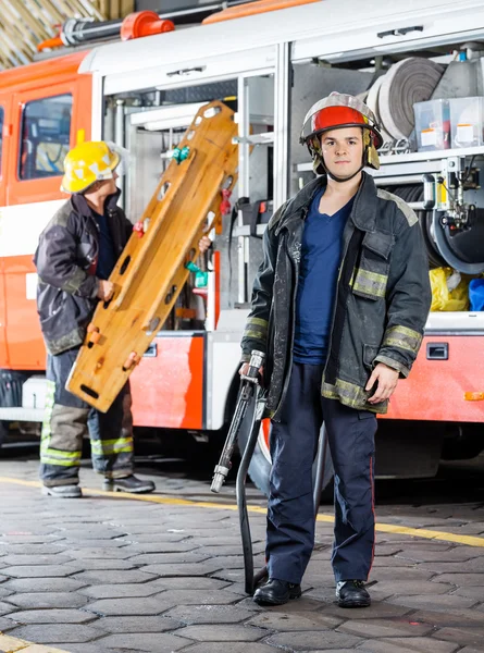 Pompier tenant tuyau tandis que collègue portant civière — Photo
