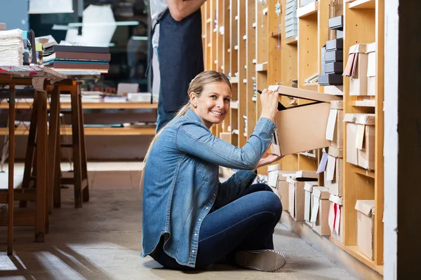 Счастливая женщина удаление коробки клиента с полки в магазине — стоковое фото