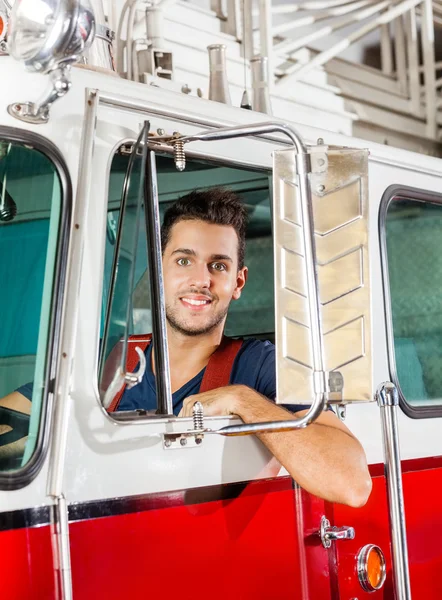Улыбающийся пожарный, сидящий в пожарном грузовике — стоковое фото