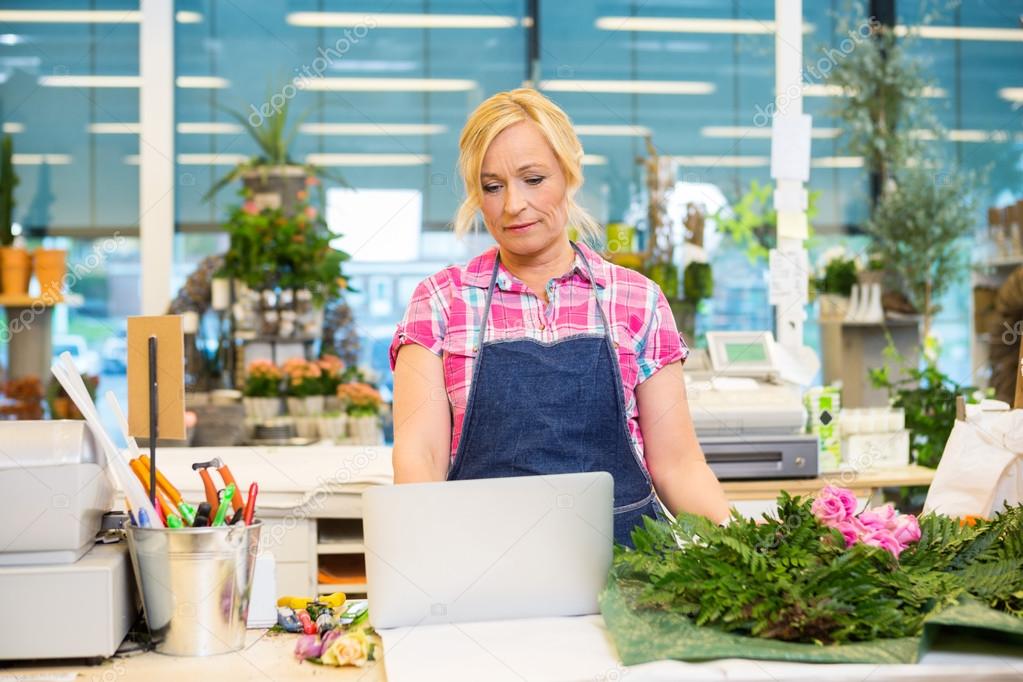 Florist Using Laptop At Counter In Flower Shop