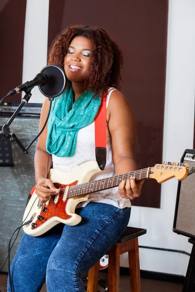 Cantora com os olhos fechados tocando guitarra no estúdio — Fotografia de Stock